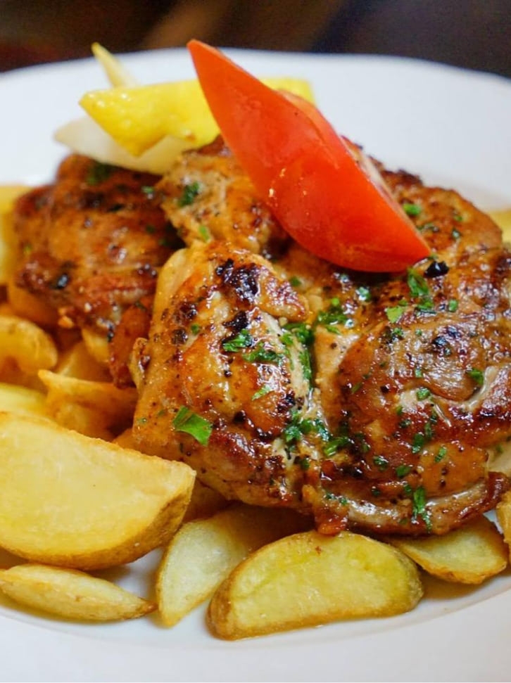 Roast chicken thighs and potato wedges served on a white plate.