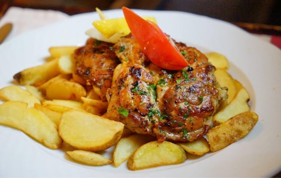 Roast chicken thighs and potato wedges served on a white plate.